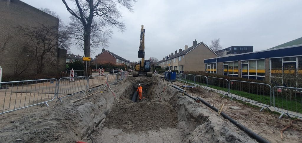 Een straat in Sluiswaard die open ligt, met een hijskraan en een bouwvakker aan het werk.