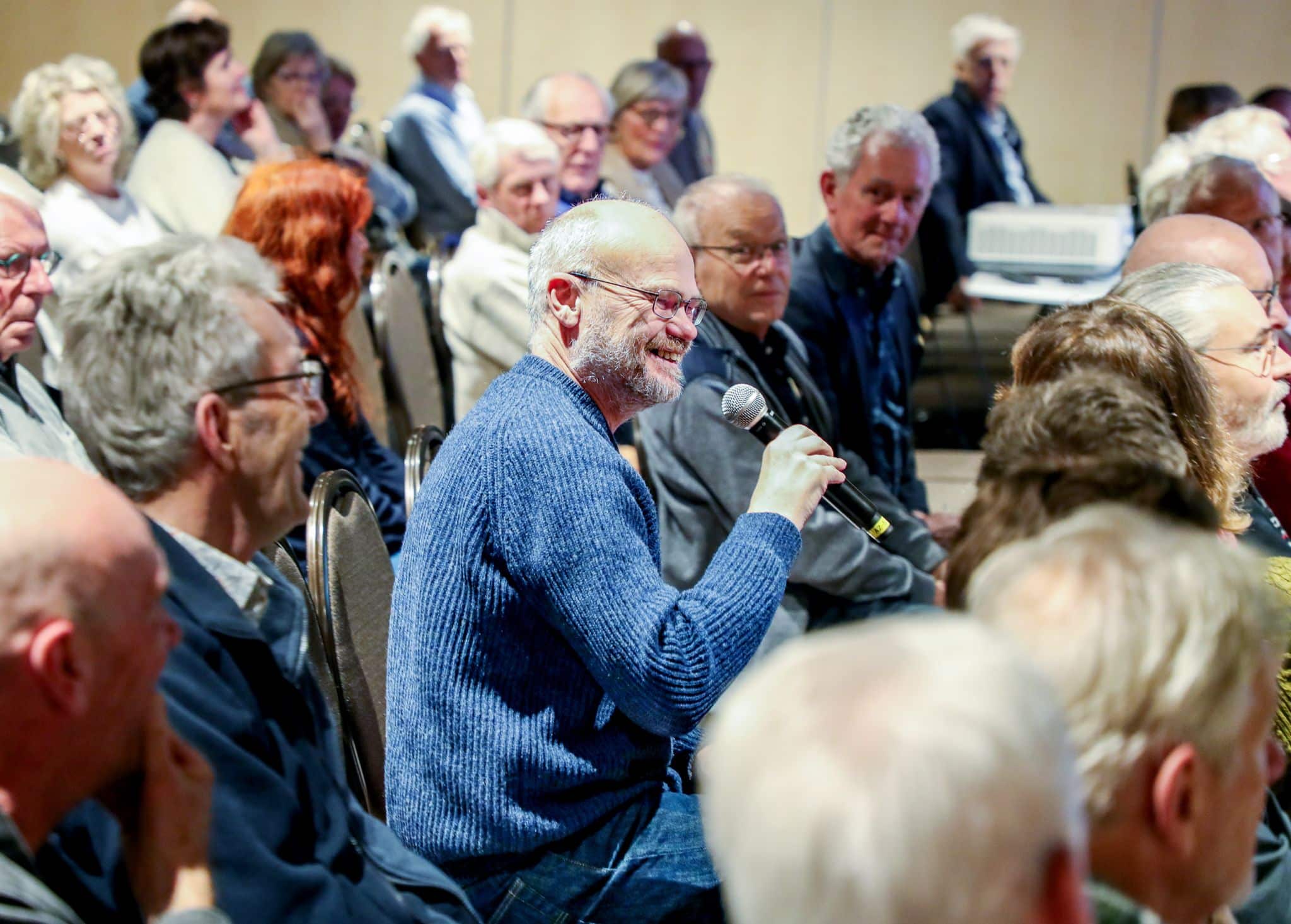 Zaal vol mensen, man uit de zaal stelt een vraag in microfoon 
