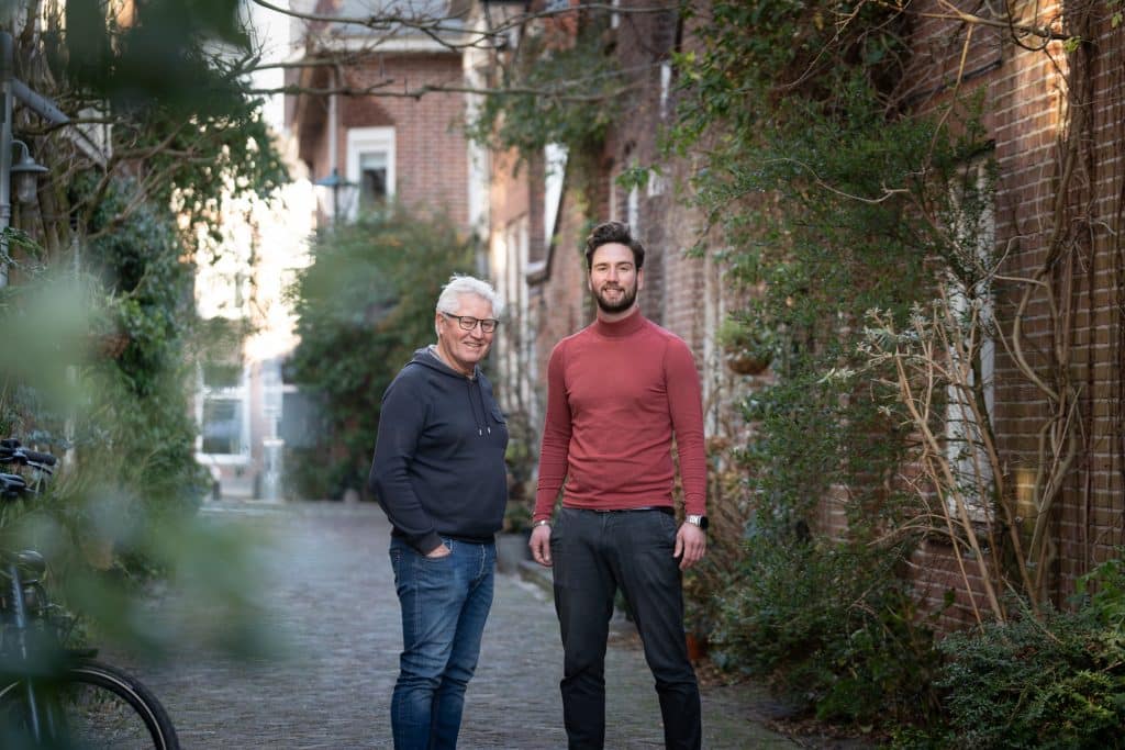 Twee mannen in een straat met veel geveltuinen en groen. Ze kijken in de camera. 