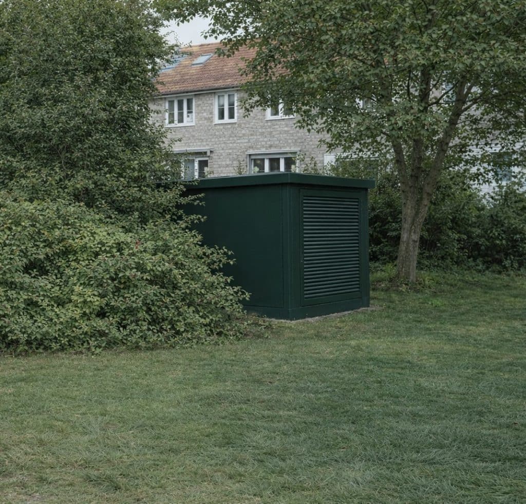 Groen elektricteitshuisje verscholen tussen de struiken. 